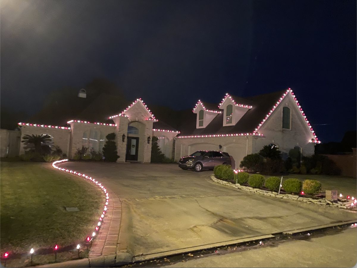 Warm-white and red C9 bulbs outlining the rooflines, gables and peaks of a two-story brick home, with lit stakes lining the front walk