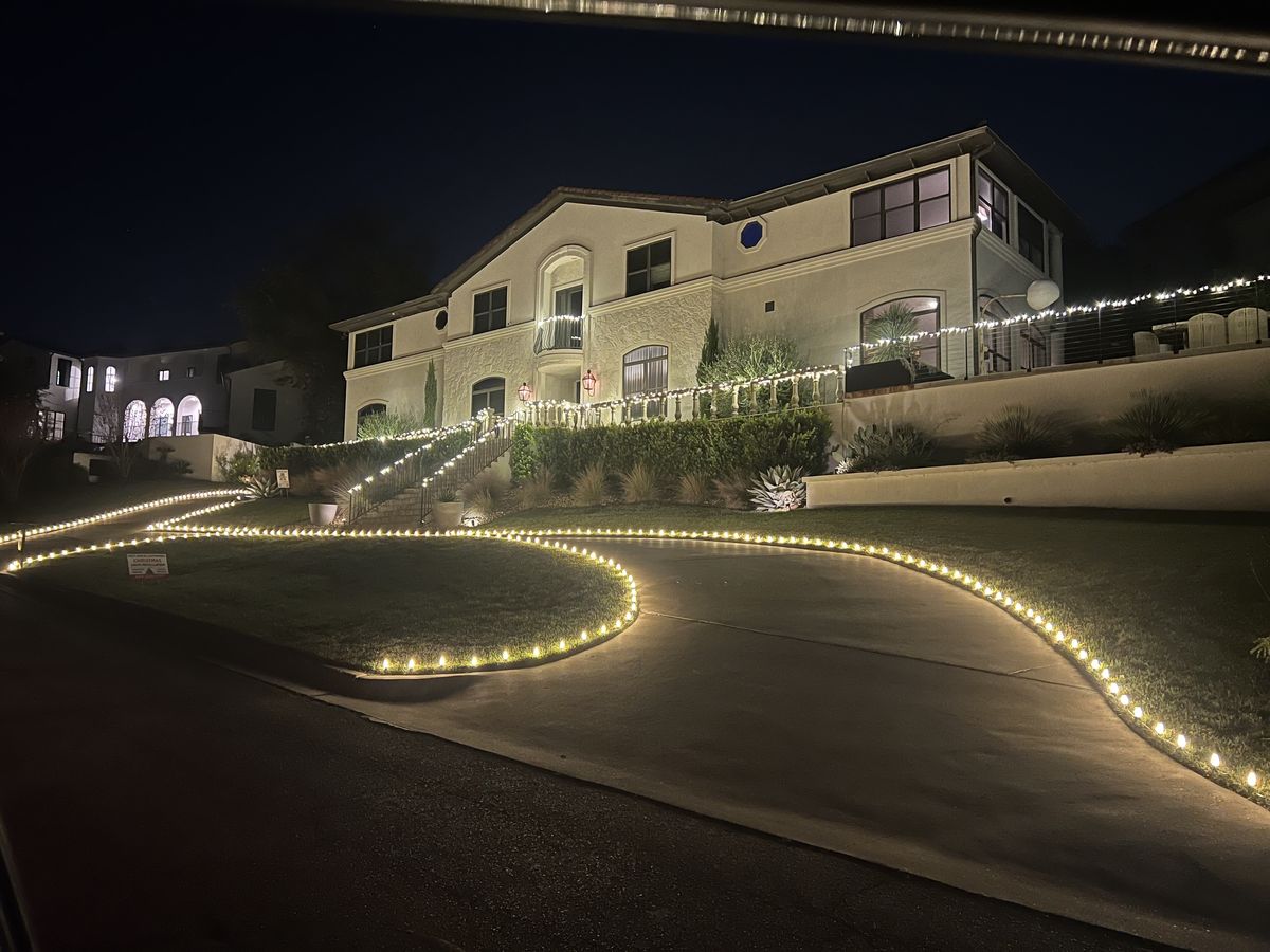 A hillside West Austin home with warm-white C9 bulbs traced along every roofline and the driveway edge lit at dusk